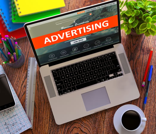 laptop on a desk with a cup of coffee - screen says "Advertising"