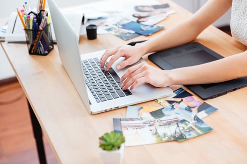 Closeup of hands of young woman typing on laptop keyboard and using graphic tablet