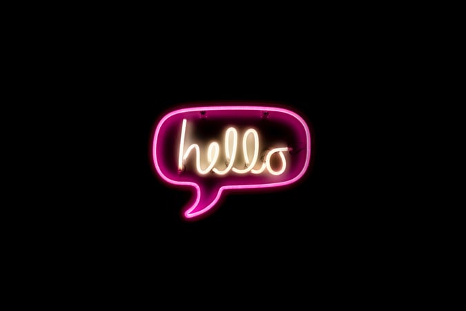 black background with "hello" written in neon light script with pink conversation bubble