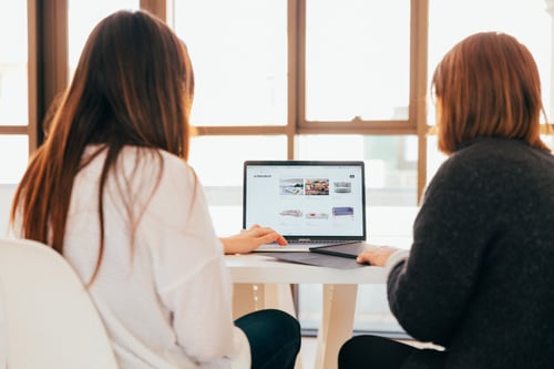 adWhite marketing Tale of the CMS Tape: HubSpot vs WordPress Two Girls Working on Laptop in Front of Windo